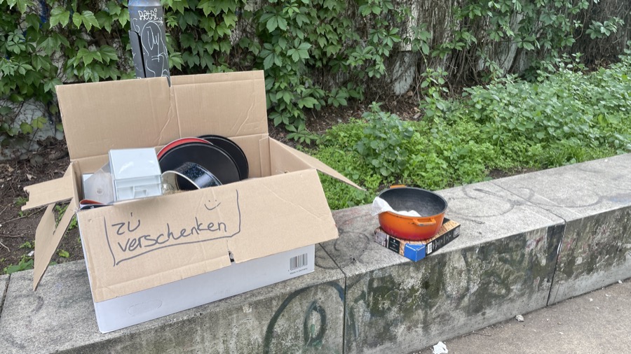 Cardboard box on a curb with kitchen items inside, labeled 'zu Verschenken' (for free) in German.